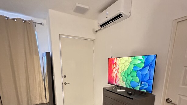 Una habitación de hotel con cama, tocador, televisor y aire acondicionado.