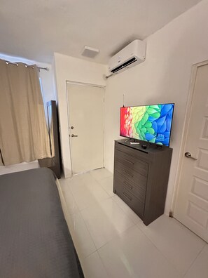 A hotel room with a bed, a dresser, a TV, and an air conditioning unit.