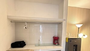Una kitchenette compacta con cubierta blanca, una cafetera y un refrigerador.
