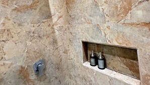 Un baño con ducha, lavamanos y estante con artículos de aseo.