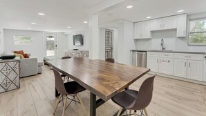 A modern kitchen with white cabinets, a wooden dining table, and a built-in oven.