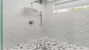 A modern shower area with a geometric tile pattern on the walls and a pebble tile floor.