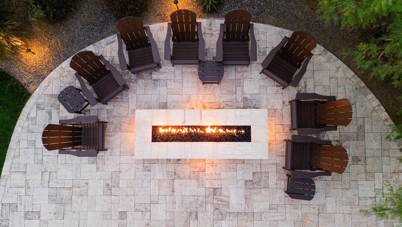 An outdoor seating area with six Adirondack chairs arranged around a rectangular fire pit.