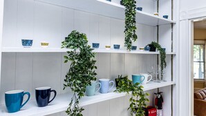 A kitchen with white shelves, blue and white cups, and green plants. - Broadway Vibes Only 1BR  2 Beds  Best Location (Somerville)