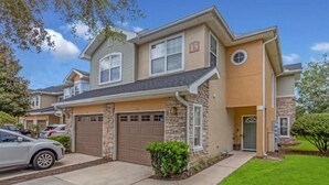 A two-story house with a stone facade, a garage, and a well-maintained lawn. - 3 Bedrooms Condos at Cottages Oakleaf (Orange Park)