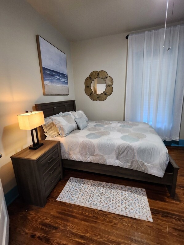 A bedroom with a bed, a nightstand with a lamp, a mirror, and a painting on the wall.