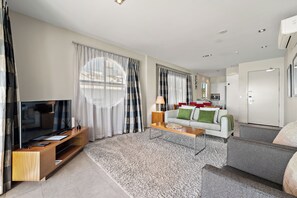 A modern living room with a flat-screen TV, a sofa, a coffee table, and a dining area in the background. - Paihia Waterfront Suites (Paihia)