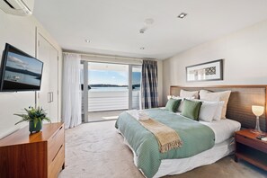 A modern bedroom with a large bed, a TV, and a view of the sea. - Paihia Waterfront Suites (Paihia)