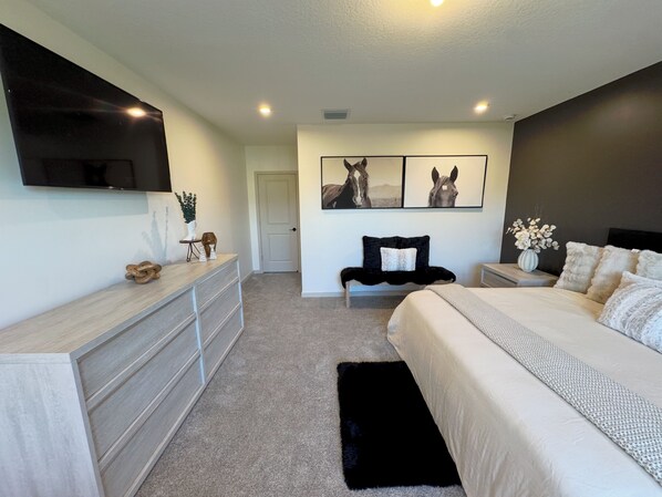 Un dormitorio moderno con cama, cómoda y televisor montado en la pared.