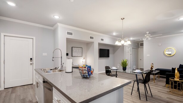 A modern kitchen with a central island, a dining area with a table and chairs, and a living area with a sofa and a TV.