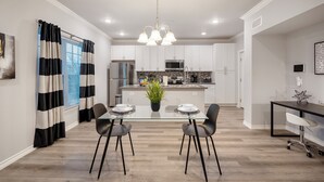 A modern kitchen with white cabinets, a central island, and a dining area with a glass table and chairs.