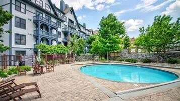 Une piscine entourée d’une terrasse en briques, agrémentée de meubles en bois et d’un mur en pierre.
