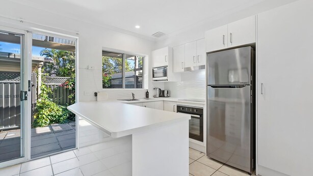 A modern kitchen with white cabinetry, a stainless steel refrigerator, and a large island. - Beachside Townhouse (Sunrise Beach)