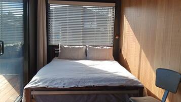A bedroom with a bed, a chair, wooden walls, and a window with blinds.