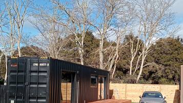 Una vivienda modular negra tipo contenedor, con una terraza de madera y un coche aparcado cerca.