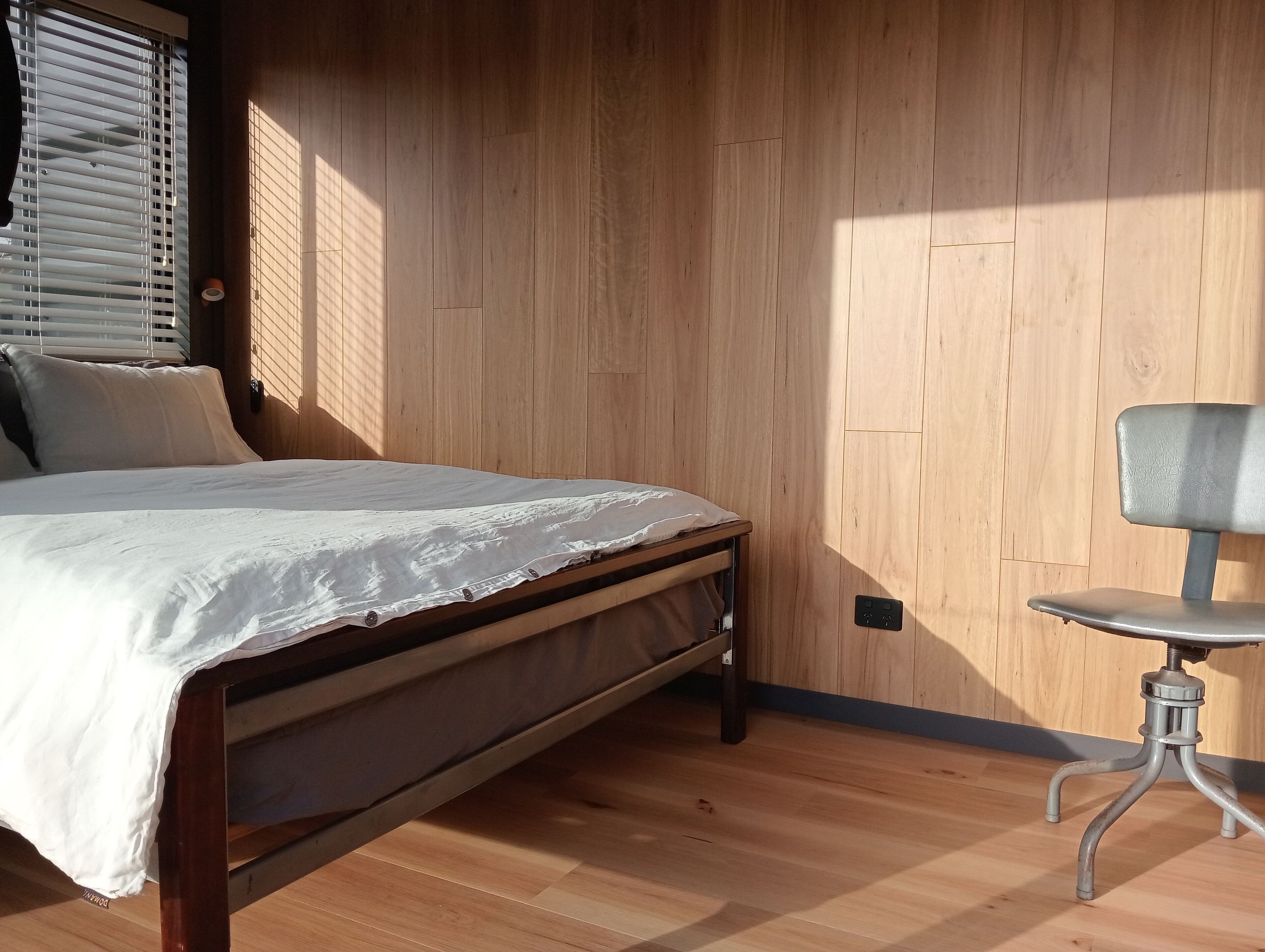 A bedroom with a wooden bed, a chair, and a window with blinds.