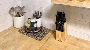 A kitchen with white tiled backsplash, wooden countertop, and various utensils and cookware organized on the counter. - Peaceful cozy cabin in the woods (Murphy)