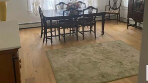 A dining area with a wooden table and chairs, a patterned rug, and a cabinet with a painting. - Charming Entire Main Floor with WiFi in downtown Hawley (Hawley)