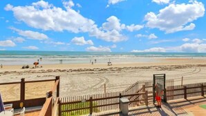 Vista de la playa con una terraza de madera, un portón y una persona de pie cerca.