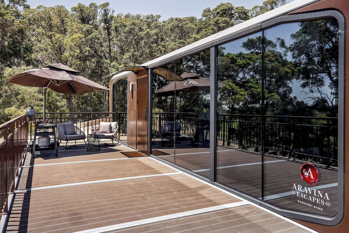 A deck with outdoor seating, umbrellas, and a glass wall offering a view of the surrounding forest.