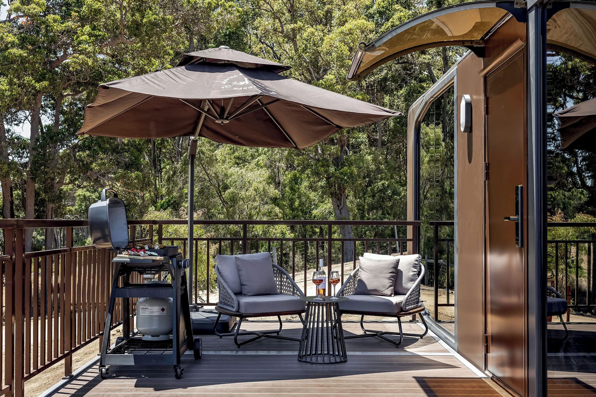 An outdoor deck with two lounge chairs, a grill, and a large umbrella.