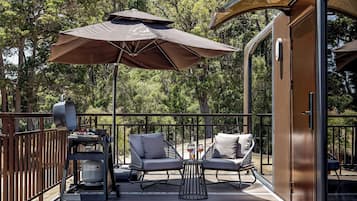 An outdoor deck with two lounge chairs, a grill, and a large umbrella.