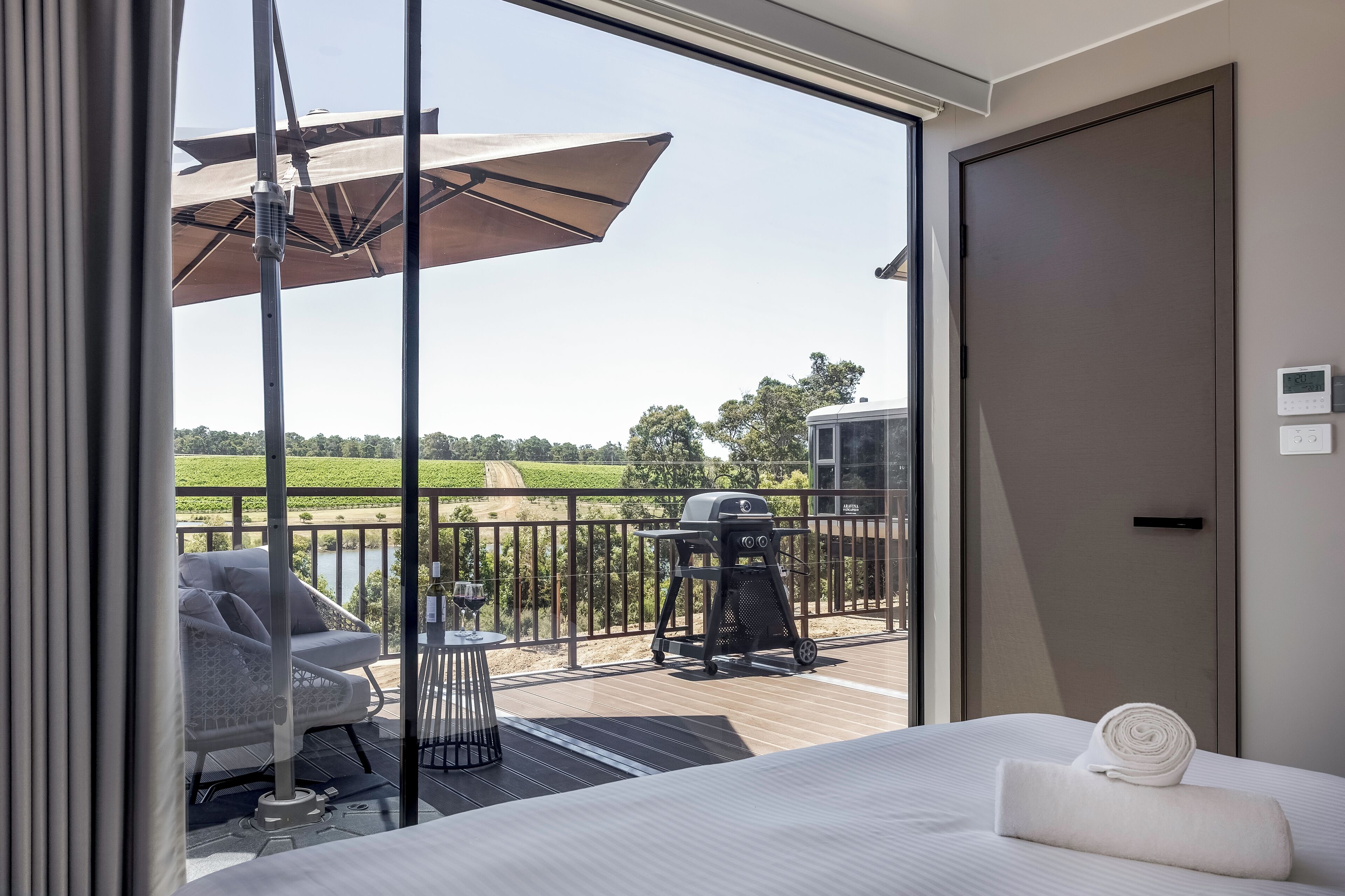 A hotel room with a balcony, a bed, a chair, a table, and a grill.