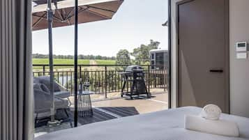 A hotel room with a balcony, a bed, a chair, a table, and a grill.