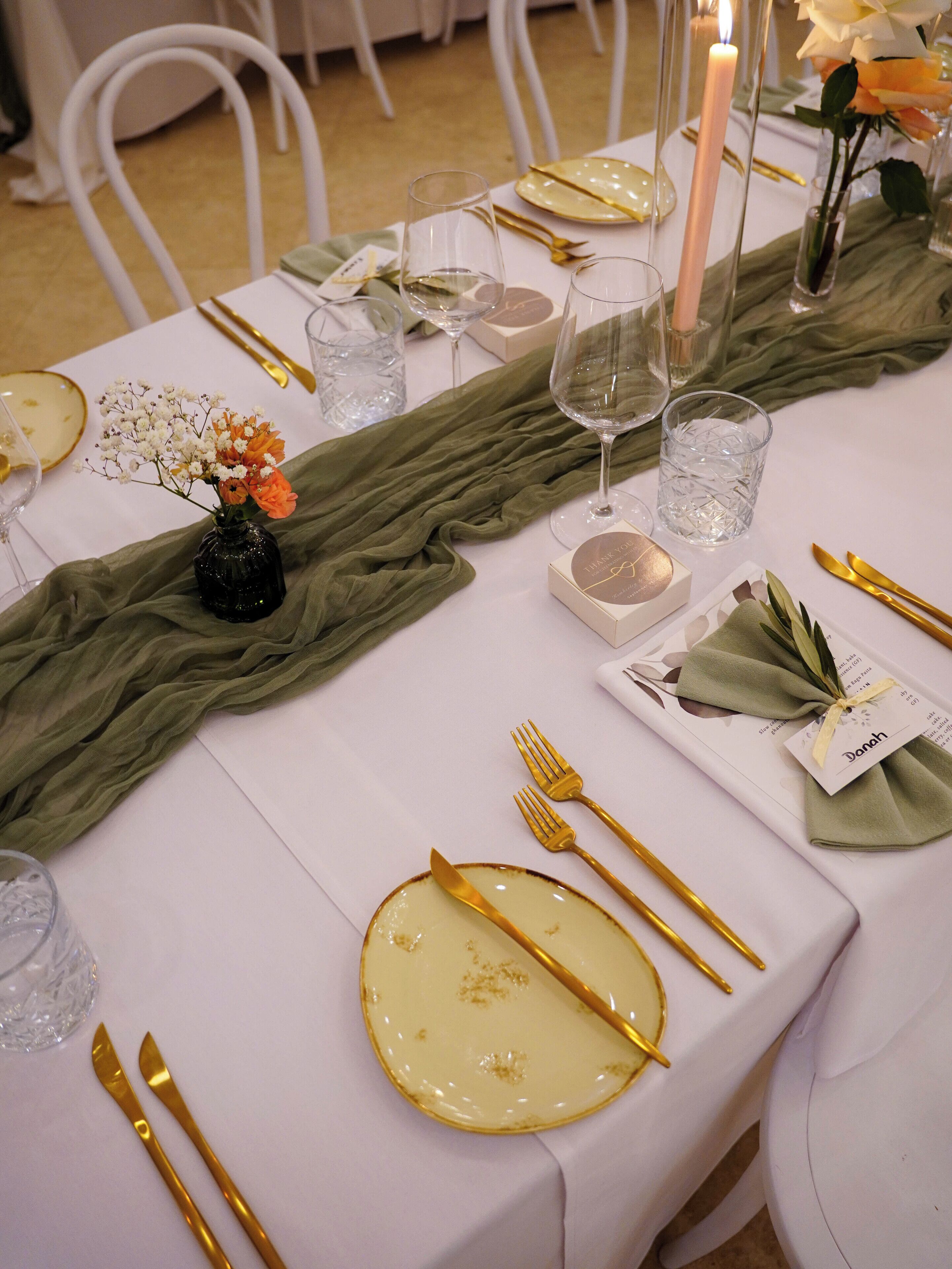 A table set with gold cutlery, a candle, and a vase with flowers.
