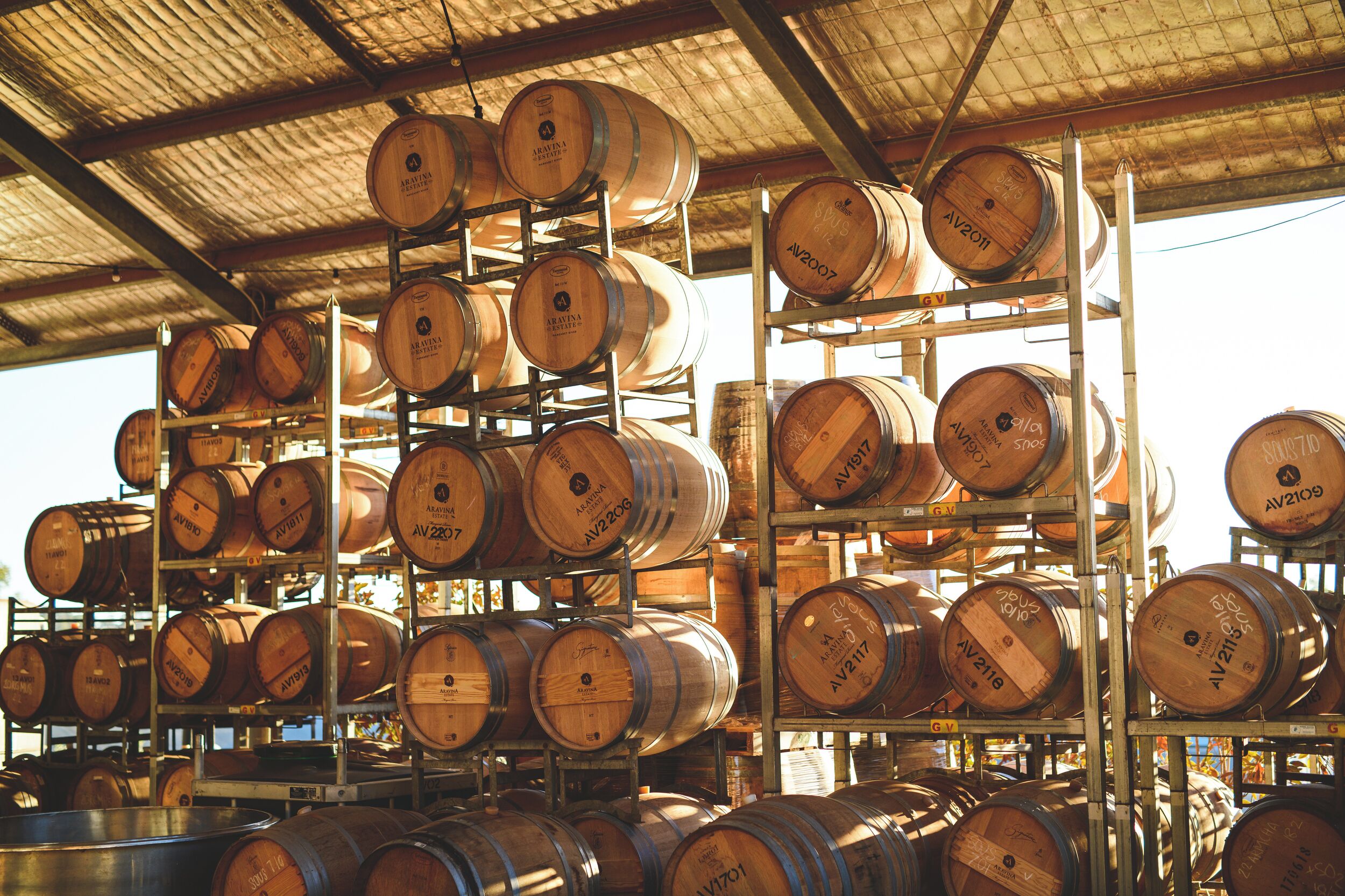 Wooden barrels stacked on metal shelves in a warehouse.