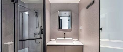 Un baño moderno con cabina de ducha de vidrio, un lavamanos blanco y un espejo.