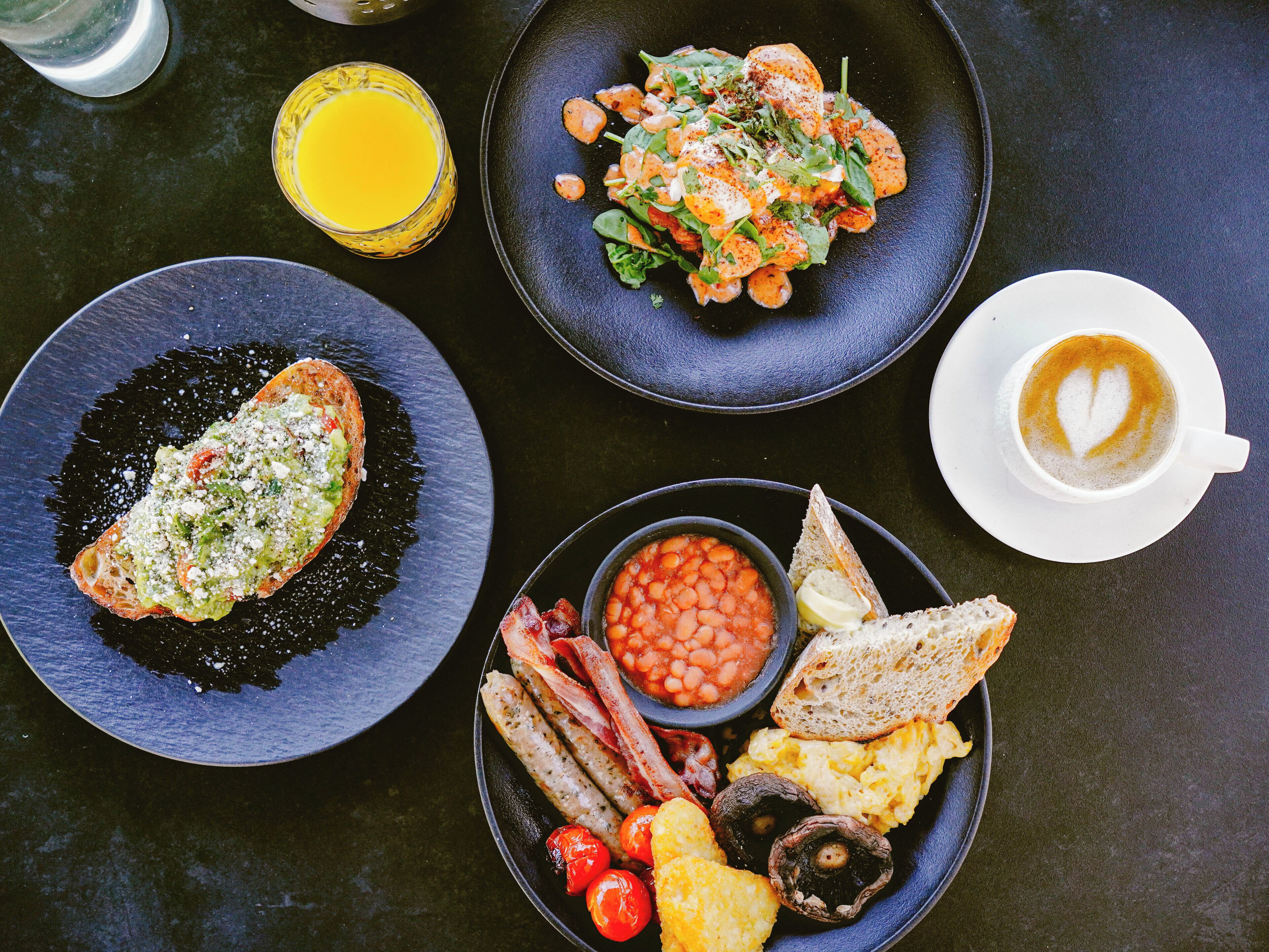 A breakfast spread with toast, beans, bacon, eggs, mushrooms, and toast on a dark table.