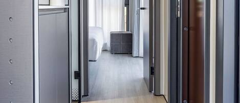 A modern hotel corridor with a neutral color scheme, a visible bed, and a small seating area.