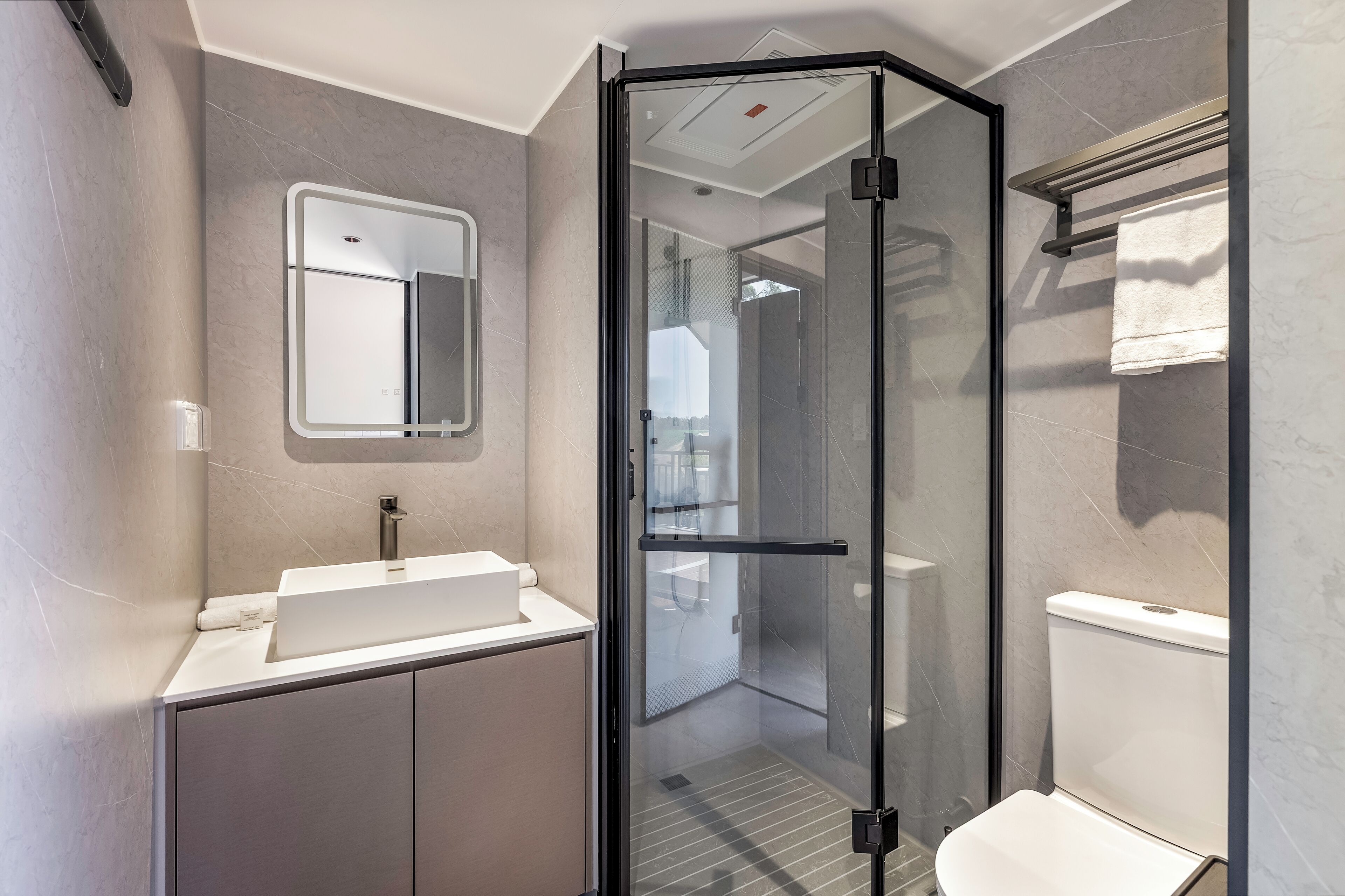 A modern bathroom with a glass-enclosed shower, a white sink, and a toilet.