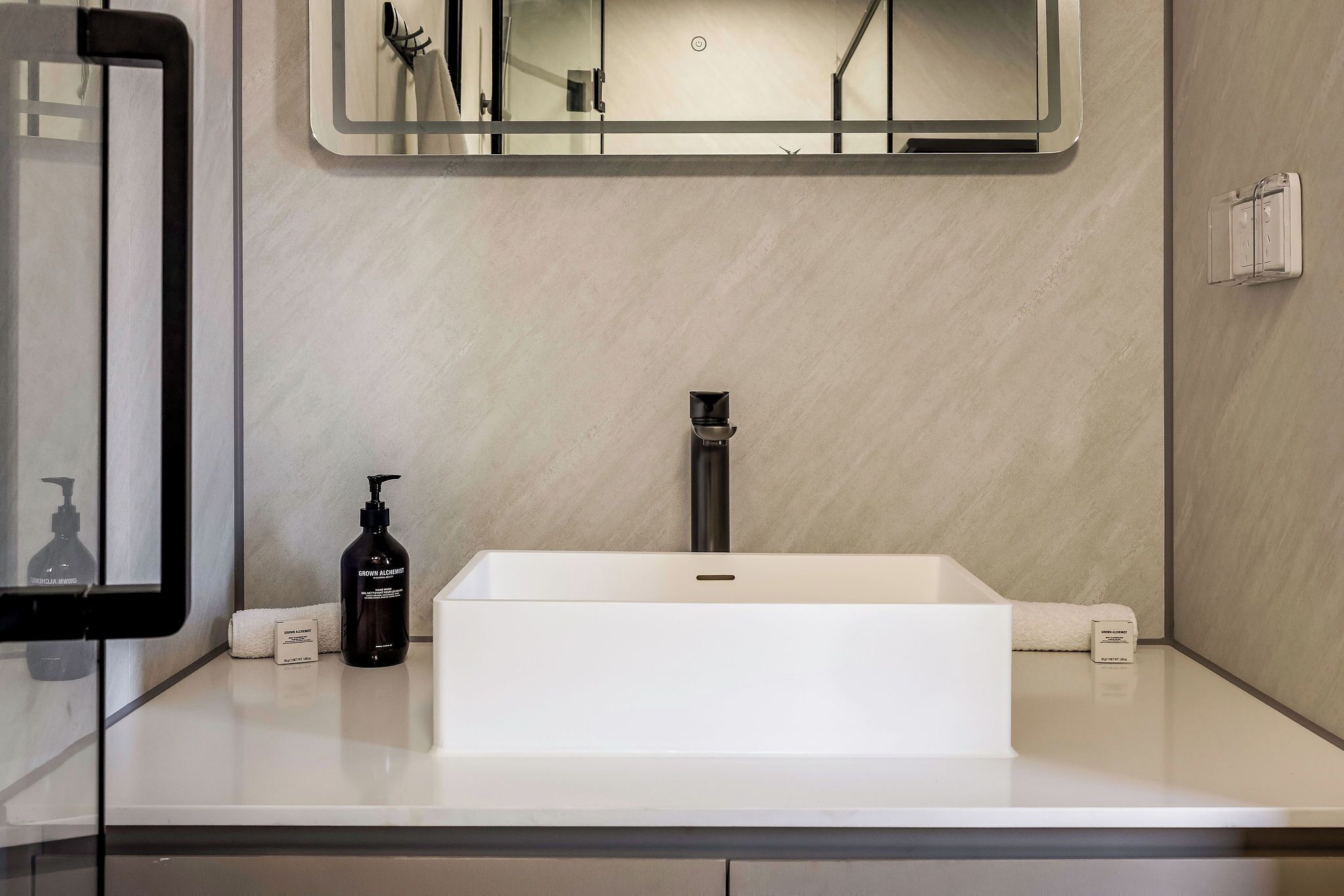 A modern bathroom with a white sink, a black bottle of shampoo, and a towel.