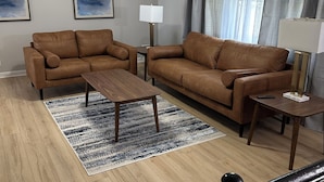 Een woonkamer met twee bruine leren banken, een houten salontafel, een vloerlamp en een plafondventilator.