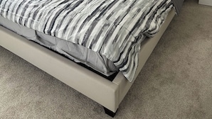 Een bed met een gestreept dekbed, een hoofdbord en een nachtkastje met een lamp.