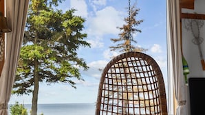 A cozy room with a wicker hanging chair by a large window overlooking a scenic view. - Megvy: Oceanfront PEI Beach House with Gazebo, Deck & Private Beach Access (Prince Edward Island)