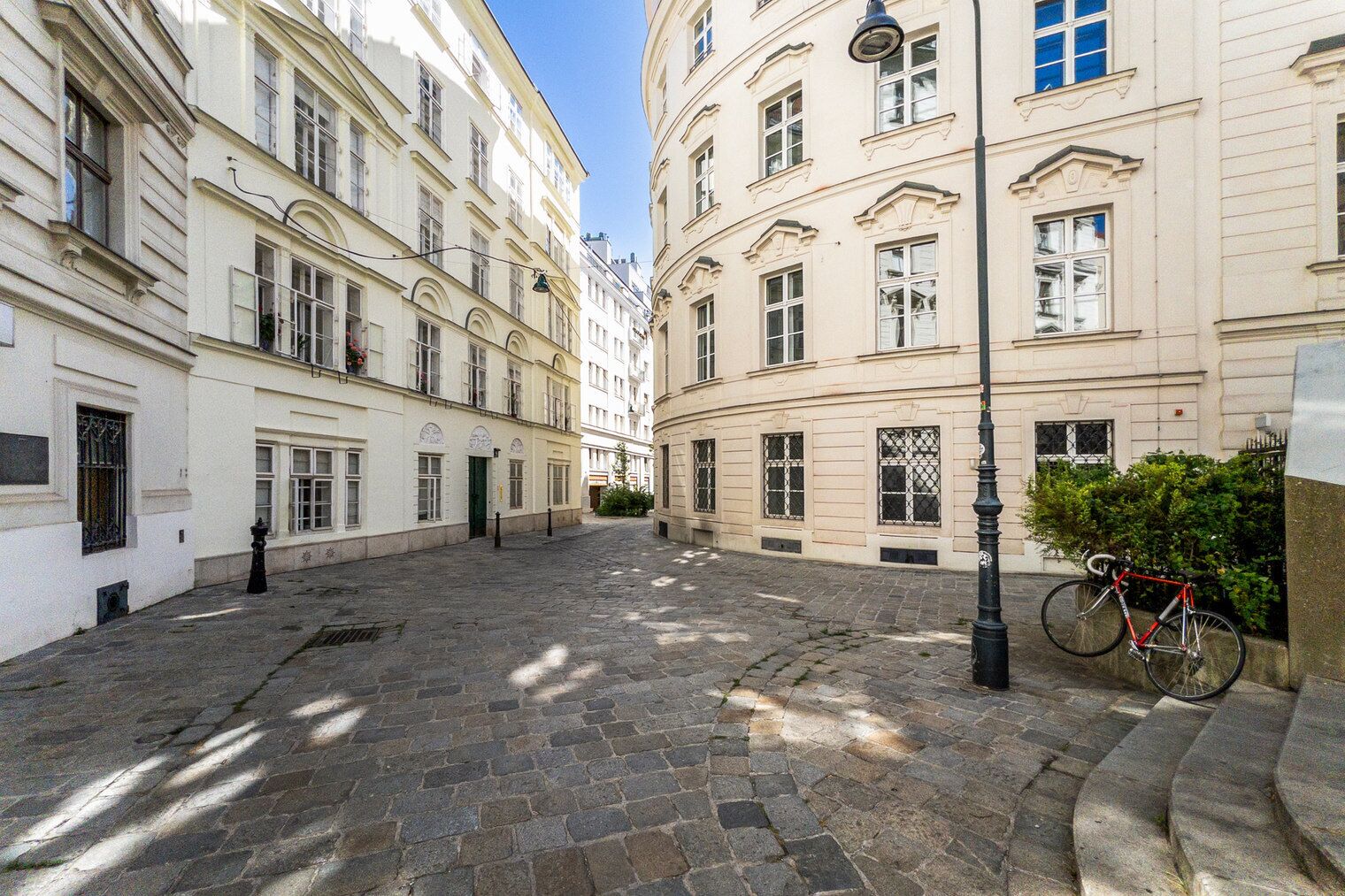 Une rue pavée, bordée d’immeubles aux grandes fenêtres, avec un vélo garé sur le côté droit.