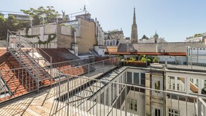 A rooftop terrace with a metal staircase, a view of a church spire, and surrounding buildings. - Blueground | Innere Stadt, w/d, nr St. Stephen's Cathedral (Vienna)