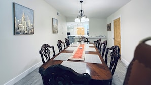 Un comedor con una larga mesa de madera, rodeado de sillas, y una cocina al fondo.
