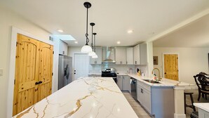 Una cocina moderna con isla de mármol, electrodomésticos de acero inoxidable e iluminación colgante.