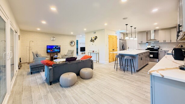 Una cocina moderna con una isla central, taburetes de bar y un área de comedor con televisor.
