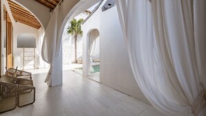 A spacious corridor with white walls and wooden beams, leading to a pool area with a palm tree and a bed. - Villa Estrella Seseh (Munggu)