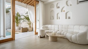 A modern living room with a sectional sofa, a round coffee table, and a stone wall with recessed shelves. - Villa Estrella Seseh (Munggu)