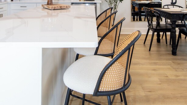 Une cuisine moderne avec des meubles blancs, un îlot en marbre et un coin repas comprenant une table ronde et des chaises en osier.