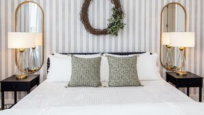 Une chambre à coucher bien aménagée, avec un grand lit, deux tables de chevet, deux miroirs fixés au mur et une guirlande décorative accrochée au mur.