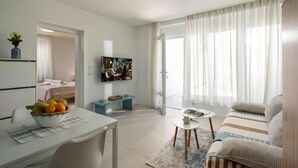Ein modernes Wohnzimmer mit einer Couch, einem Esstisch mit Obstschale, einem Fernseher und einem großen Fenster mit Vorhängen.