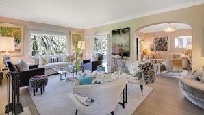 A spacious living area with a sofa, armchairs, and a coffee table. There is a large window providing natural light and a view of greenery outside. - Riviera Gem - Designer decorated private 2BR home (Santa Barbara)