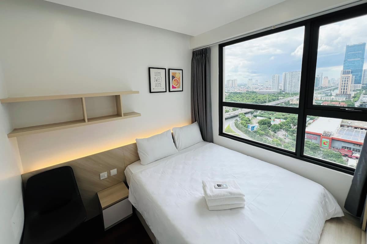 Une chambre d’hôtel avec un lit, un bureau, une étagère et une fenêtre donnant sur la ville.